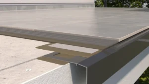 Zbliżenie krawędzi tarasu z płytkami ceramicznymi zamontowanymi na profilu okapowym K301, z widoczną warstwą zaprawy klejowej i podkładem cementowym.