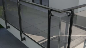 Szklana balustrada balkonowa z aluminiowymi słupkami i pochwytami, zamontowana na krawędzi balkonu przy nowoczesnej elewacji.